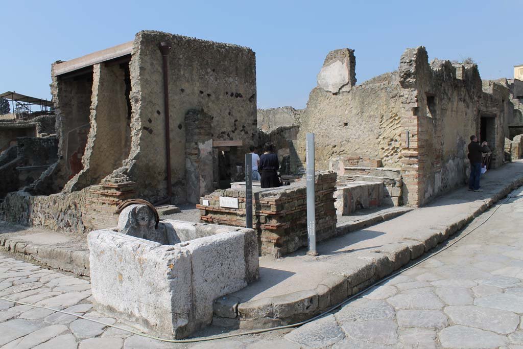 Cardo V Inferiore, Herculaneum. May 2010. 
Looking south towards fountain on corner of Ins. IV, at junction of Decumanus Inferiore, on right, and Cardo V Inferiore, on left. 
Entrance doorway to bar at IV.16, on the right
.
