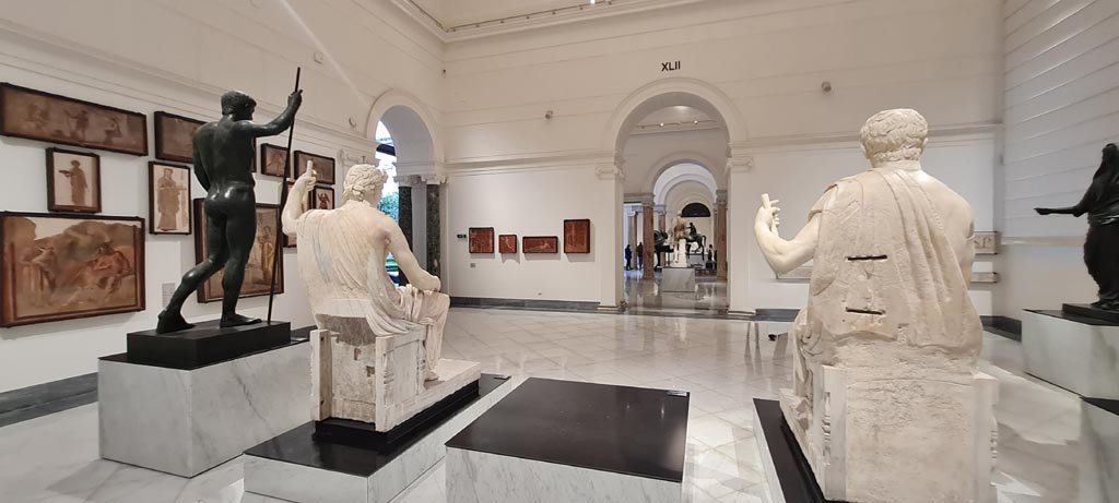 Herculaneum Augusteum. April 2023. 
Looking across display from rear of statues in “Campania Romana” gallery in Naples Archaeological Museum towards paintings on left of Arch. 
Photo courtesy of Giuseppe Ciaramella.
