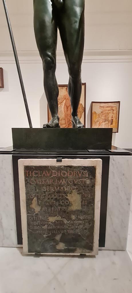 Herculaneum Augusteum. April 2023. 
Bronze statue of Claudius, above, with Bronze plaque, below – a Dedication to Claudius, inv. 3718. 
Photo courtesy of Giuseppe Ciaramella.
