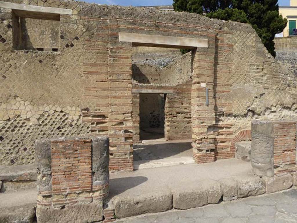 II.2 Herculaneum, October 2014. Looking west towards doorway. Photo courtesy of Michael Binns.
According to Pagano, “Although this has not been totally uncovered, at least one can judge that this would have been a large dwelling, and was given this name by the finding of a fresco showing the shepherd Argo who protects the nymph Io. On the outside we see two long benches at the side of the door, in front of which the masonry pilasters covered in stucco held up a roof. This door, as well as in the preceding house, was not the main entrance but knowing the manner of building/construction of the ancients, this must have been found on the opposite side which is not yet excavated.
Firstly, it presents a room somewhat preserved with beautiful walls painted in red with architectural drawings and pictures of marine views. The floor is in white mosaic, with large window on the left protruding over the garden. 
The garden or peristyle has a beautiful colonnade around which held the roof of the portico. Several of the columns still retain their capitals of white stucco very well worked with taste. 
Around the portico there are many rooms, and the one seen in the first portico on the left entering, with walls painted in red and floors of white mosaic, called an exedra or reception room which was without doors, and according to the use of the ancients, would have been closed with a curtain of cloth.
Another large room for the same use seen in the portico on the right, which was also decorated with paintings and marble floor. Presently, there are just traces remaining. Then, you go to another room for dining with large window protruding to the garden. It has walls painted in red and architectural designs”.
See PAGANO, N, Descrizione degli scavi di Ercolano, 1870. (p.22-25)

