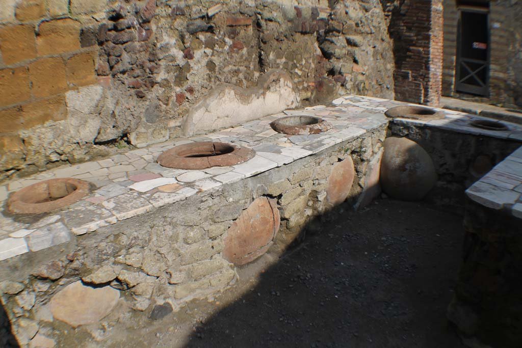 II.6 Herculaneum. March 2019. Looking north-west from rear of masonry counter/podium.
The counter is faced with sheets of marble and embedded with dolia, which would have contained the liquids and foodstuff.
The doorway at II.7 is on the north side of the counter/podium (top right) and entered from the Decumanus Inferiore.
Foto Annette Haug, ERC Grant 681269 DÉCOR.

