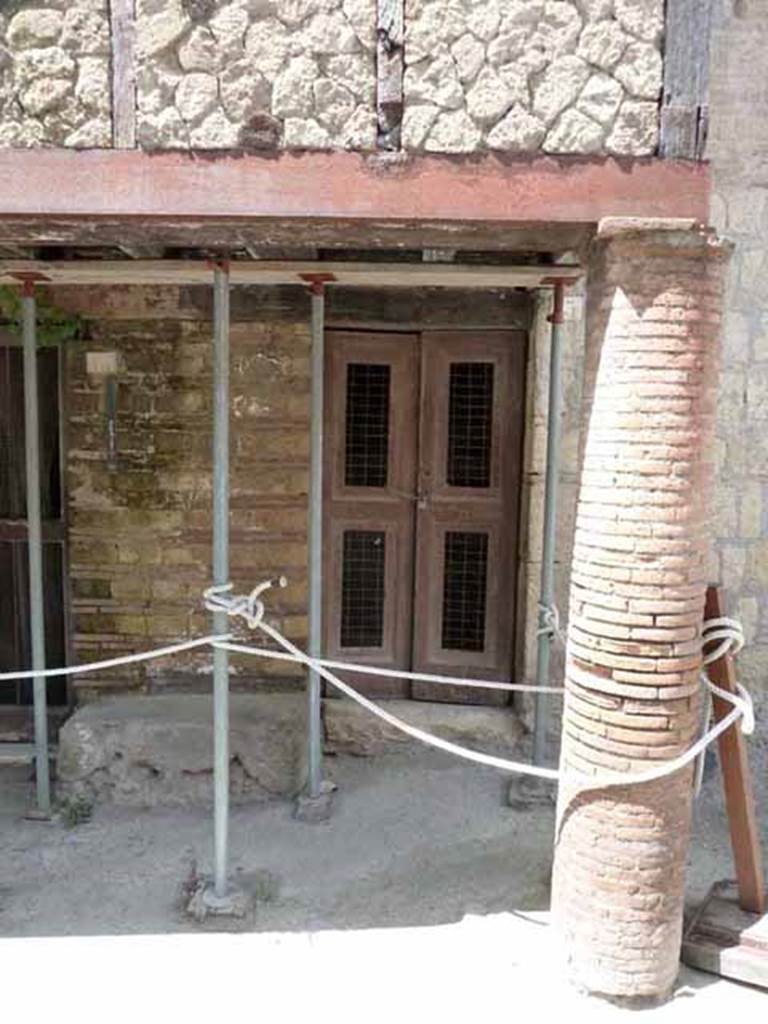 III.13, Herculaneum. May 2010. Doorway to the steps to upper floor, set under the balcony supported by brick columns.
