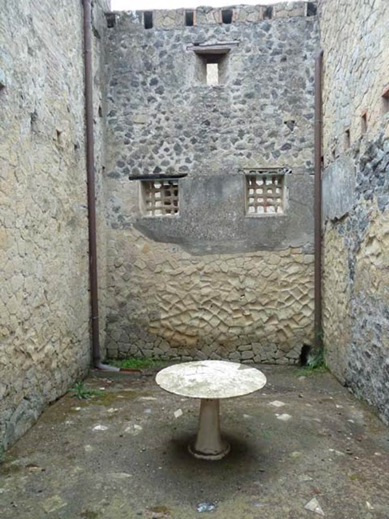 IV.4 Herculaneum. September 2015. 
Room 18, looking towards west wall with two windows with iron gratings to protect the windows.
In the south and north walls are support beams for an upper floor. 
At the top of the west wall are the holes for the support beams for another upper floor.
In the middle of the room is a white marble circular table.

