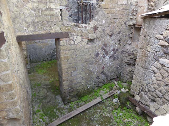 IV.19 Herculaneum, October 2014. 
Looking south towards to doorway of room 6, rooms at rear of IV.19, photo taken from room 16 the triclinium of IV.4.
On the right side of this photo can be seen the wall at the rear of the latrine in the House of the Stags, next to it is
the latrine for IV.19 which would be in the corner near the piece of wood and bits of stones.
Above the latrine is a large pipe from the upper floor that discharged water into the drain well which was communal to both houses.
Photo courtesy of Michael Binns.

