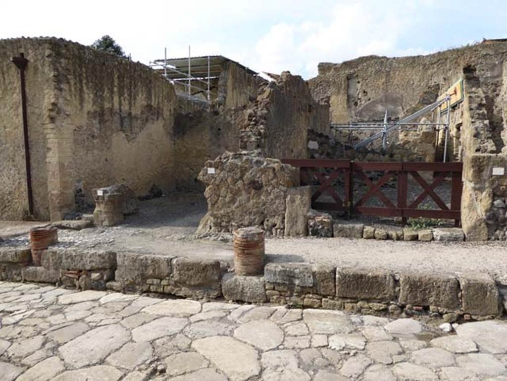 V.27, on left, and V.26, on right, Herculaneum, October 2014. Looking west on Cardo V. Superiore. These entrance doorways would have been sheltered under a portico, but only a small portion of the columns remain preserved in the pavement. Photo courtesy of Michael Binns.
