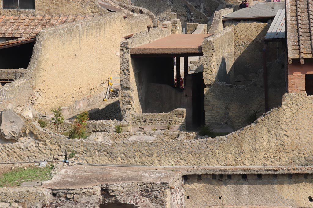 Ins. Or. I.1, Herculaneum. October 2023. Photo taken from access roadway.
Looking north at west end, on the left is the ruined Diaeta 12 opening onto the collapsed loggia.
Behind them are the terrace area, and ruined rooms 8 and 7. The room with flat roof in shadow is the kitchen. 
The unroofed room on the right of the kitchen is room 3, not yet photographed. Photo courtesy of Klaus Heese.
