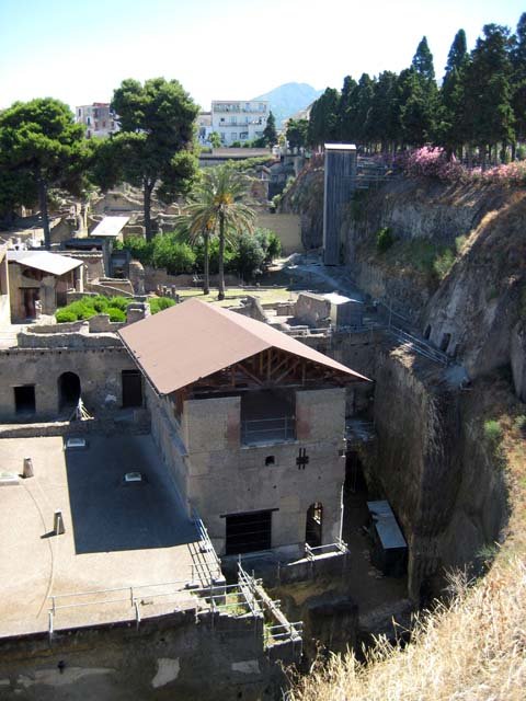 Herculaneum, June 2012. On the left is the Terrace of Balbus and east end of the arched openings to the boatsheds, below.  On the right is the Suburban Baths, with the “tower” room of the House of Relief of Telephus, on the extreme right.  Photo courtesy of Michael Binns.
