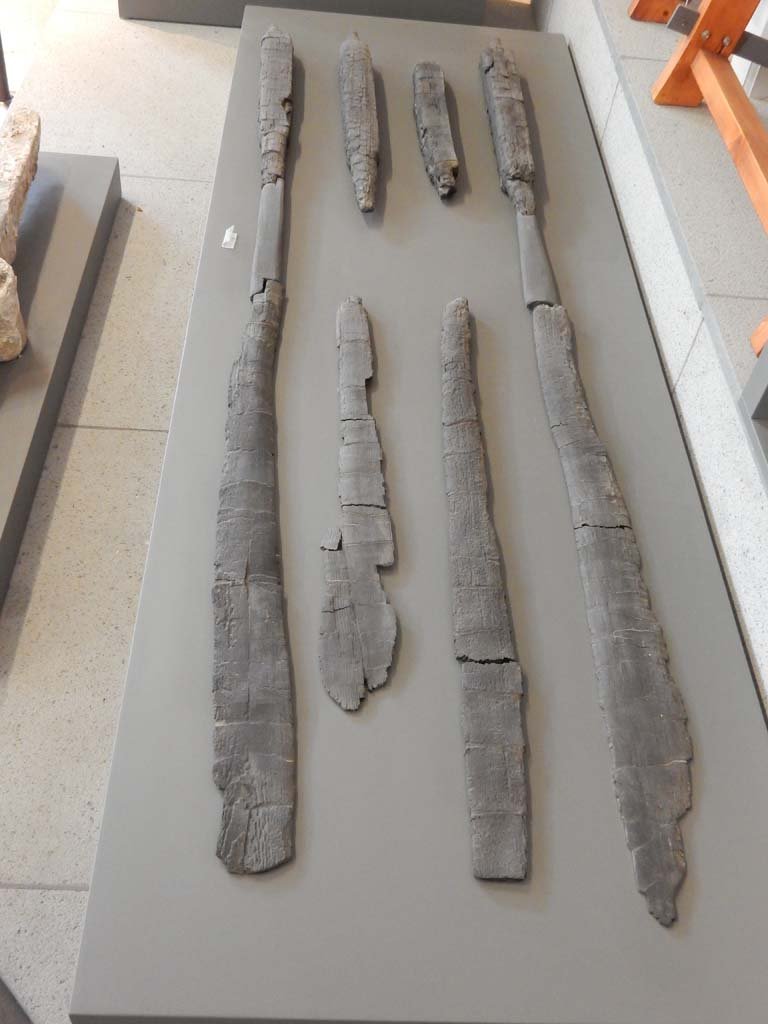 Herculaneum, June 2019. Carbonised wooden oars. 
Six oars were found in the bath building in Insula Occidentalis at Herculaneum, along with parts of other boats, a red prow in the shape of a serpent, a wooden rudder and a pile of planking ready for use. This shows that the bath building was not in use at the time of the eruption but had been transformed into a space for laying-up boats and storing maritime equipment.  Photo courtesy of Buzz Ferebee.
