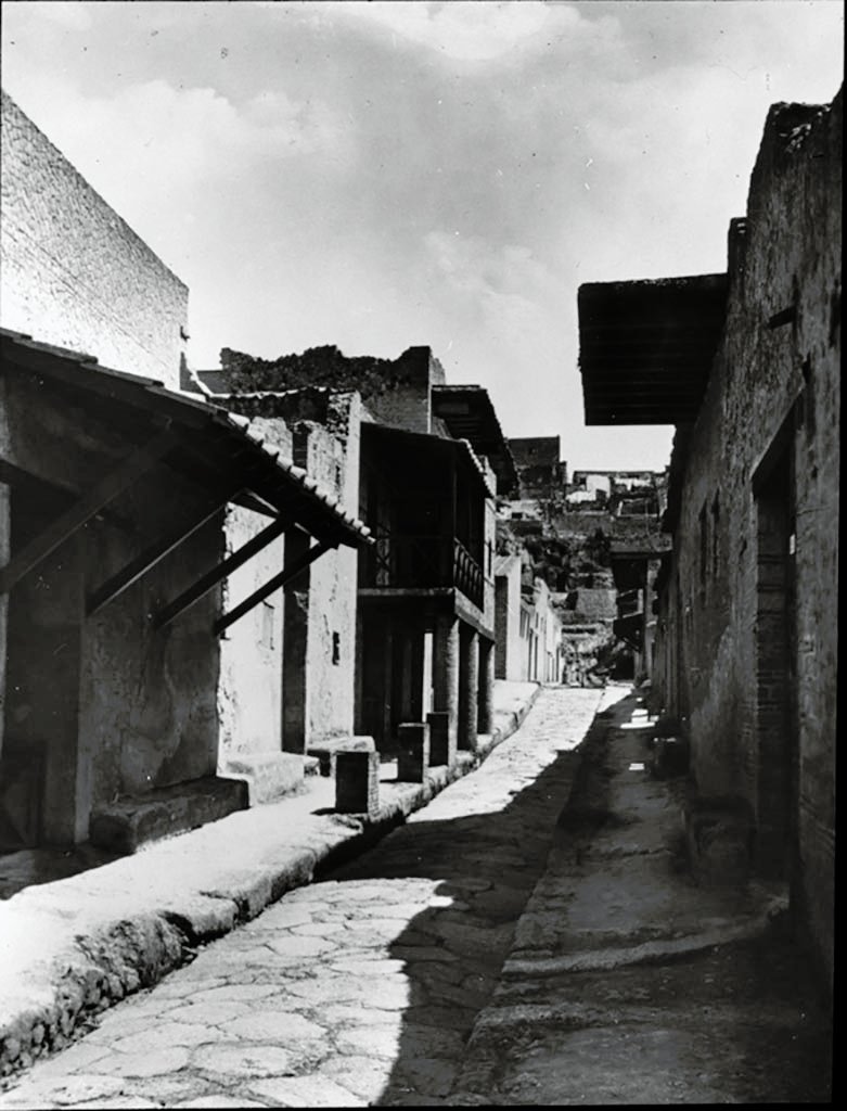 Cardo IV Inferiore, Herculaneum. 1935. Photo by Fratelli Alinari (I.D.E.A.). Alinari No 43137 (1935) oN.
Looking north from III.17, Casa dell’ Ara Laterizia or House of the Brick Altar, on left, and IV.2, Casa dell’ Atrio a mosaico or House of the Mosaic Atrium, on right.  
The colonnade in the centre of the photo is outside III.14, Casa a Graticcio or House of the Wattle Work (Opus Craticium).
Used with the permission of the Institute of Archaeology, University of Oxford. File name instarchbx116im013 Resource ID 42232.
See photo on University of Oxford HEIR database
