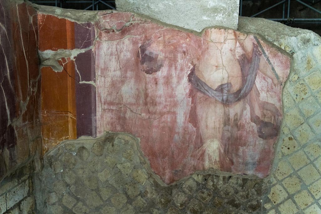 Herculaneum Villa dei Papiri. October 2023. 
North-west corner of triclinium, room (i), and north wall with painted scantily clothed figure. Photo courtesy of Johannes Eber. 
According to Moormann, this shows a tall woman, standing in front of a red background, of which some fragments have been found in room (i). 
She wears a cloak moved by the wind and holds a thin branch rod, probably a thyrsus, with the left hand against the shoulder. 
The height of the fragment, almost one metre, is an indication to classify the figure as a fragment of a megalography. 
I refer again to the specimen of Terzigno which is contemporary. 
The decoration adorns a luxurious triclinium, overlooking the sea, and brings to the villa the aspect of a pastime caught during a moment of relaxation, that is the otium. 
We have such a situation more or less equal to that of the famous room (5) of the Villa of the Mysteries in Pompeii, from which visitors could look towards the sea through a porch.
See Moormann E. M., 2009. Pitture parietali nella Villa dei Papiri a Ercolano: Vecchi rinvenimenti e nuove scoperte, in Vesuviana. Archeologia a confronto. Atti del Convegno internazionale (Bologna, 14-16 gennaio 2008), pp. 159, Fig. 8.


