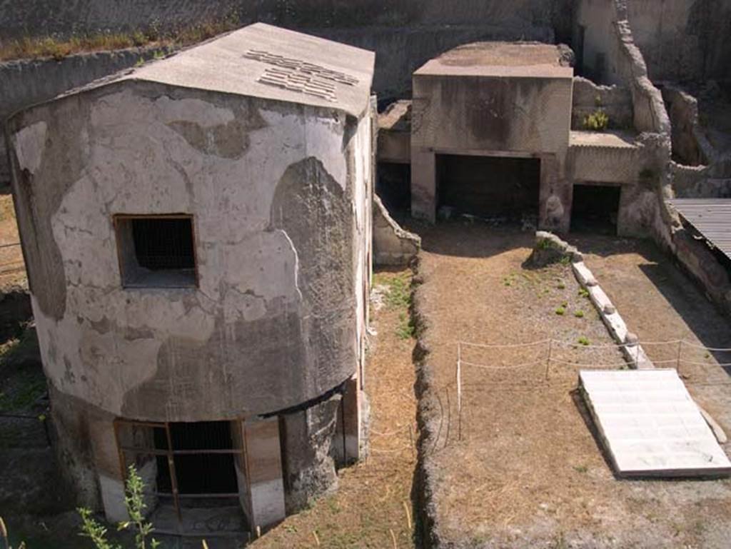 South-western baths, Herculaneum. July 2010. 
Looking towards baths complex 1, on left, separated by the adjacent terrace 2, with the lower level of large residential property, on right.
Photo courtesy of Michael Binns.
The three windows with their pyroclastic materials on the south side can be seen.
In the semi-circular apse, there would have been another three windows.
In the upper wall of the apse was a smaller rectangular window for light.
There were another three windows on the north side.
The terrace would have been bordered on the south and east by a portico, with flooring of cocciopesto with white tesserae dots.

