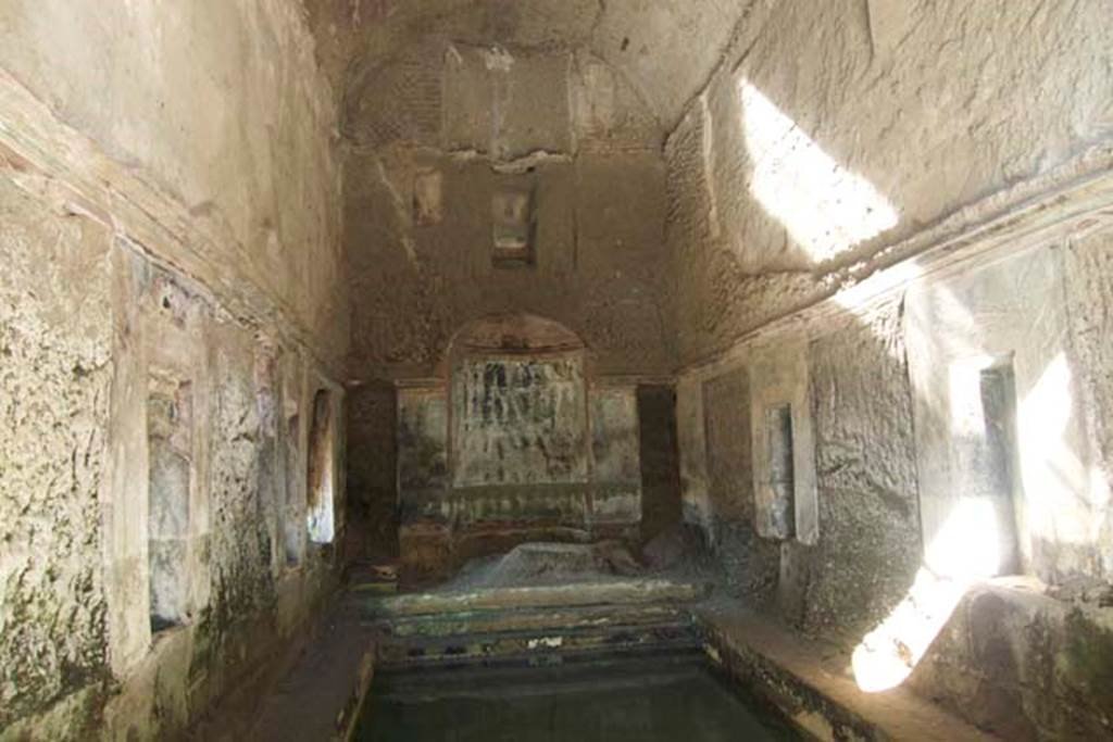 South-western baths, Herculaneum. July 2010. Room 1, interior of baths complex.
Photo courtesy of Michael Binns.
At the north end of the hot pool was a nymphaeum.
On either side of the nymphaeum would have been a narrow doorway into room 3 and other rooms of the baths complex.
Also, on the short, north side of the pool were steps descending into the water. 
On the two long sides of the pool were a total of six rectangular windows, three on each side.
These have not yet been cleared of their pyroclastic material.
There are rectangular niches visible between the windows.


