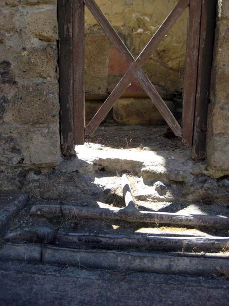 V.9 Herculaneum, June 2011. Looking east to doorway, across lines of lead pipes in pavement.
A pipe connects with the house. Photo courtesy of Sera Baker. 

